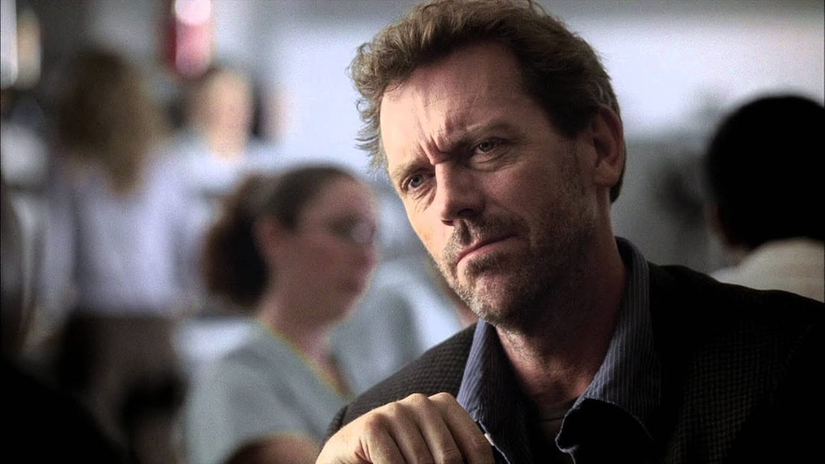 House wears a dark shirt and looks unimpressed.