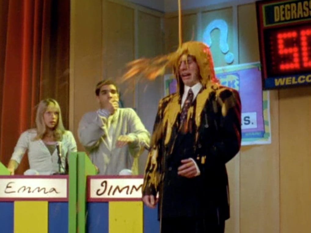 Boy in glasses and suit is slimed with yellow fluid like Carrie at the prom. He's at a trivia competition, his teammates Jimm