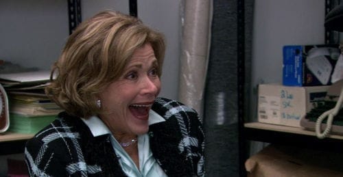 Lucille Bluth reacts with delight, wearing plaid jacket.