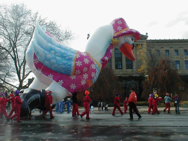 Diant duck balloon "wearing" pink with daisy pattern and a hat tilts over in Philly's Logan square