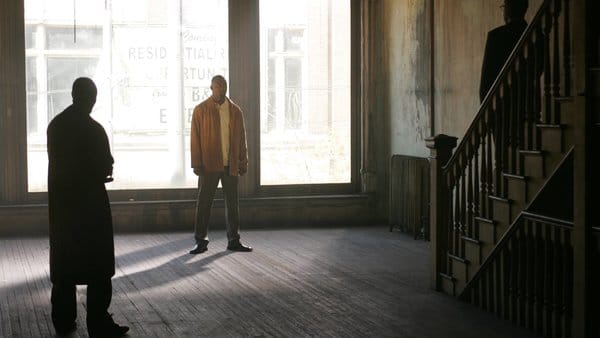 Stringer (center, brown jacket) stands in front of a woman and looks at two men with guns pointed at him