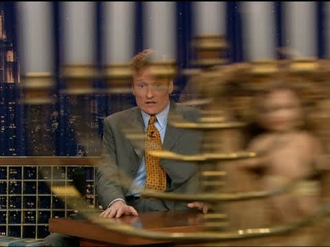 the world's fastest Menorah zips in front of Conan O'Brien (gray suit, orange tie)